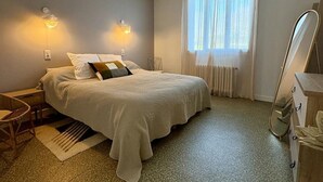 A bedroom with a bed, two wall-mounted lights, a window with sheer curtains, a wooden nightstand, a chair, and a mirror. - Spacious Home with Garden, WiFi, and Games Room Near Dordogne's Best Sights (Payzac)