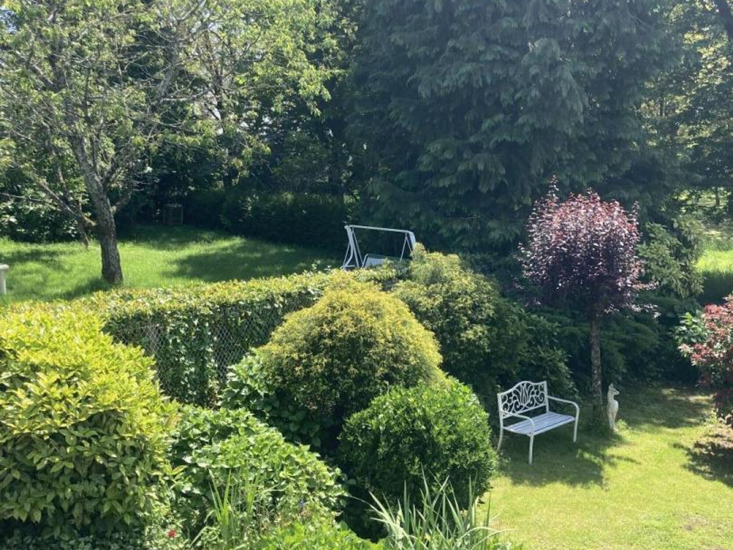 A garden with neatly trimmed hedges, a metal bench, and a swing set.