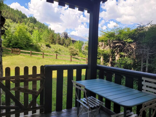 Una terraza de madera con una mesa y sillas, con vistas a una zona verde con una valla de madera y árboles.
