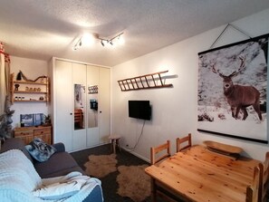 A cozy living room with a wooden dining table, a sofa, a TV mounted on the wall, and a deer poster.