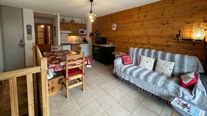 A cozy living room with a wooden wall, a sofa, and a dining table with chairs. - Super Duplex in Vars - 2 Bedrooms, Terrace, Parking (Vars)