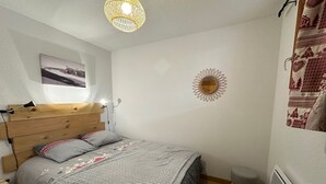 A bedroom with a wooden headboard, a bed with grey bedding, a small stool, a wall-mounted mirror, and a hanging light fixture. - Super Duplex in Vars - 2 Bedrooms, Terrace, Parking (Vars)