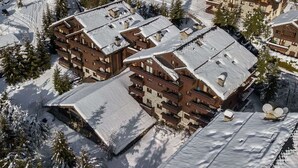 A snow-covered resort with multiple buildings, including a lodge with balconies and a ski lift visible.