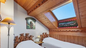 A cozy room with wooden walls and a sloped ceiling, featuring a skylight, a bed with white bedding, a lamp, and a Christmas-themed wall decoration.