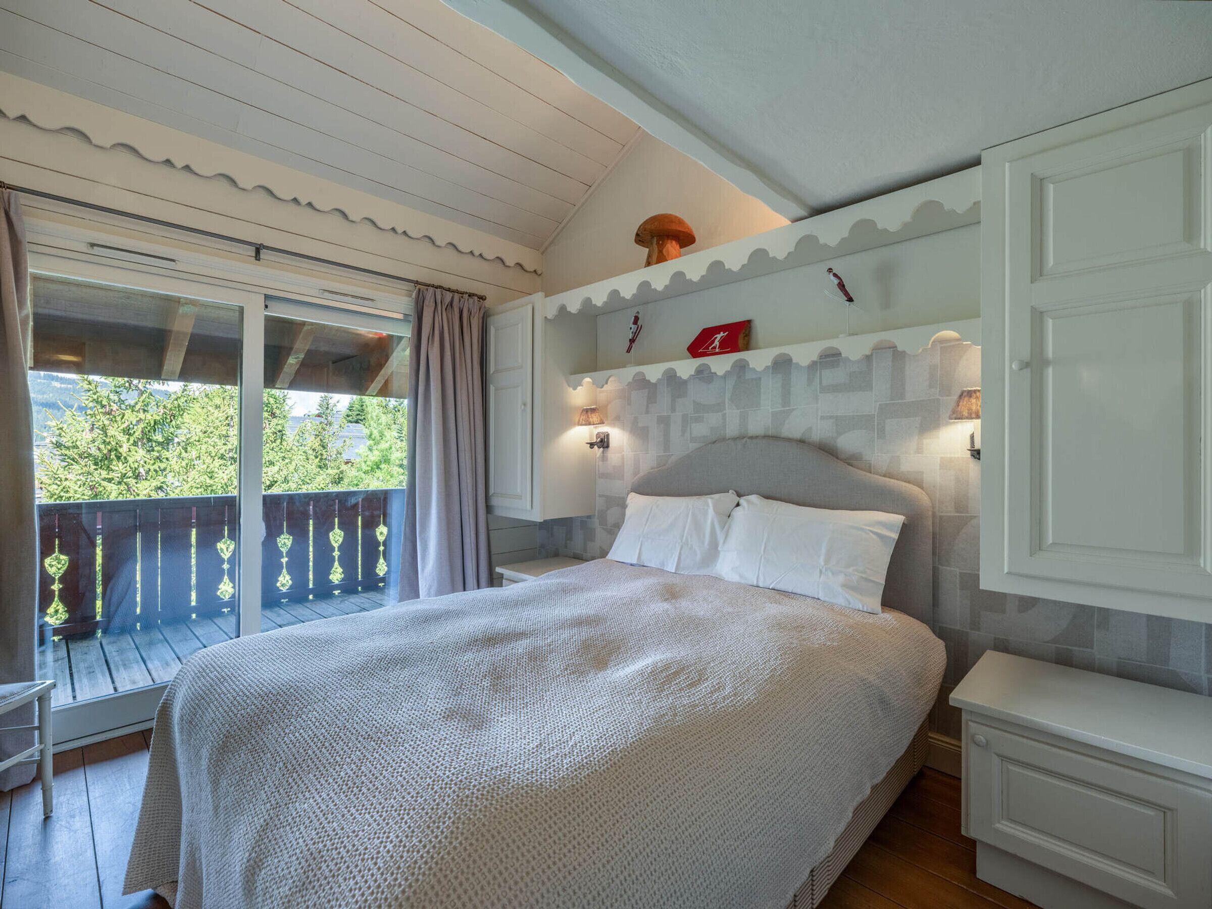 A bedroom with a large bed, a window with curtains, a balcony, and a wall with decorative elements.