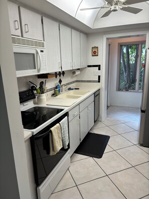 A kitchen with white cabinets, a microwave, a stove, and a sink. There is a window with a view of trees.