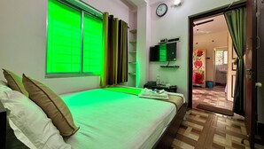 A hotel room with a bed, a TV, a clock, and a bathroom visible through an open door. - Green Place Guest House (Bankura)