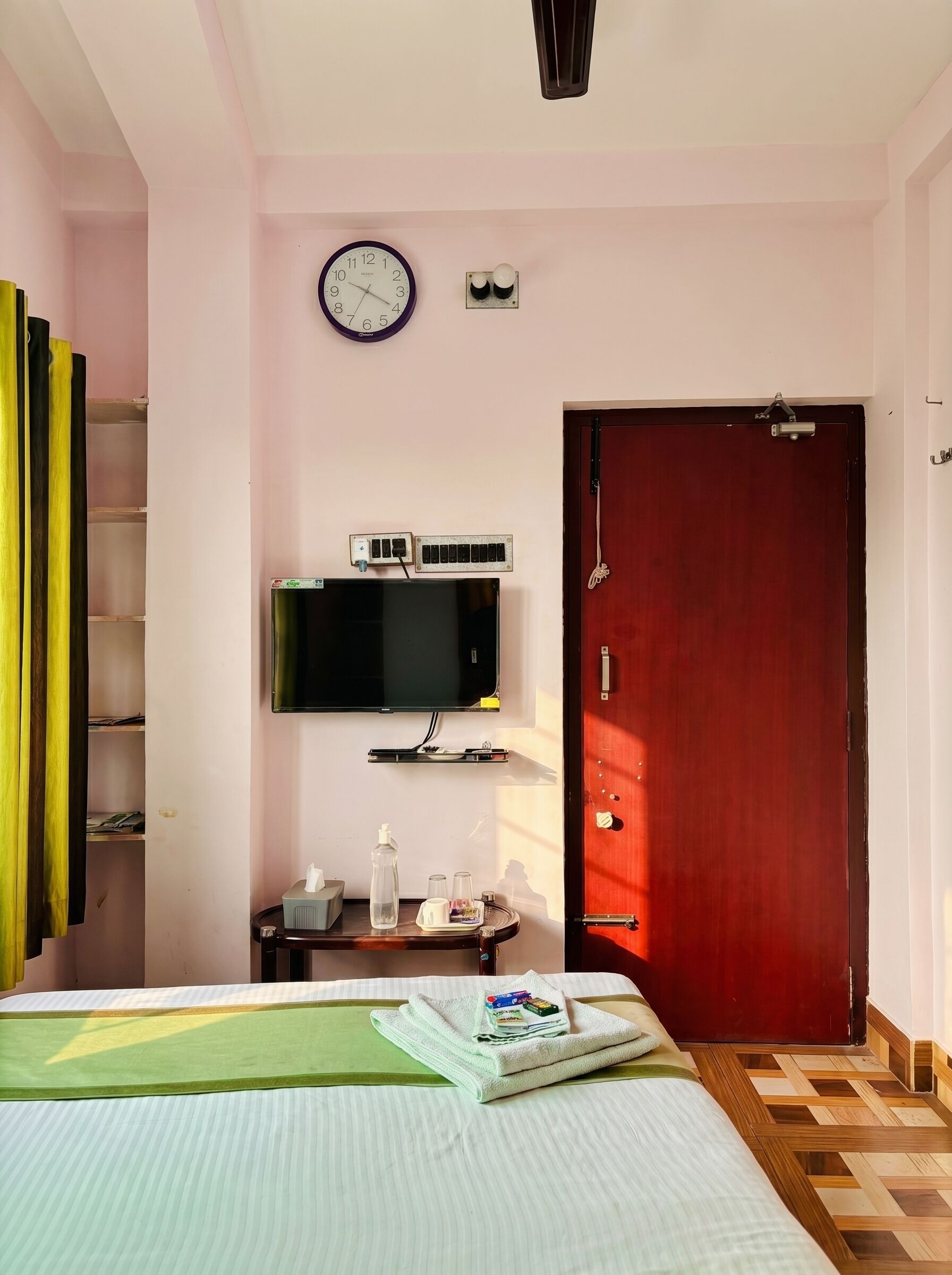 A bedroom with a bed, a television mounted on the wall, a door, and a clock.