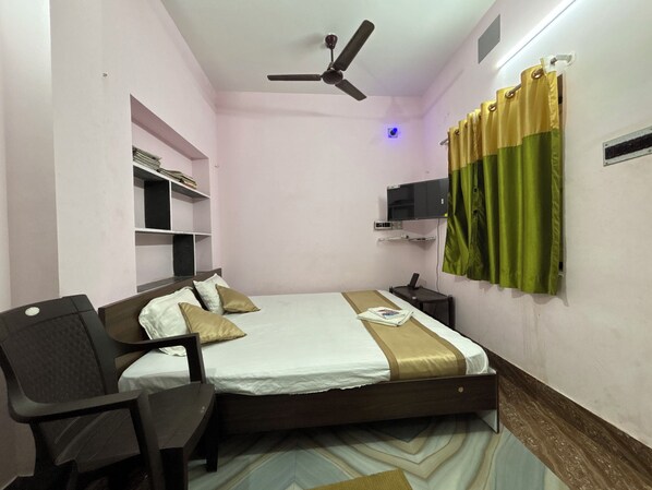 Une chambre à coucher comprenant un lit, un bureau, une chaise, un ventilateur de plafond, une télévision et une étagère remplie de livres.