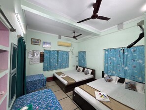 Une chambre de dortoir avec trois lits, un ventilateur de plafond, un appareil de climatisation et une carte accrochée au mur.