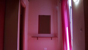 A hallway with a pink wall, a door on the left, a window on the right, and a light fixture above the door. - Appartamenti nel Centro Storico di Siculiana (Siculiana)