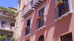A pink building with balconies, potted plants, and a sign advertising a bed and breakfast. - Appartamenti nel Centro Storico di Siculiana (Siculiana)