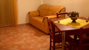 A room with a sofa, a wooden dining table with chairs, and a vase of flowers on the table. - Appartamenti nel Centro Storico di Siculiana (Siculiana)
