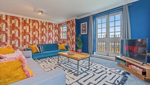Un salon avec un canapé bleu, une table basse, un téléviseur et un mur orné d’un motif.