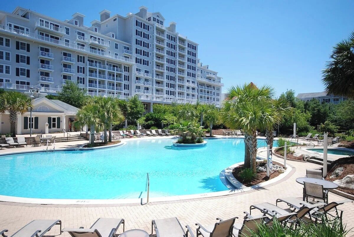 A hotel with a large swimming pool surrounded by palm trees and lounge chairs.