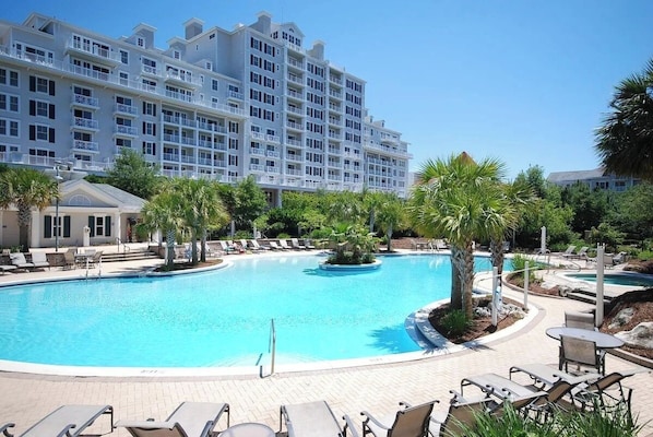 A hotel with a large swimming pool surrounded by palm trees and lounge chairs.