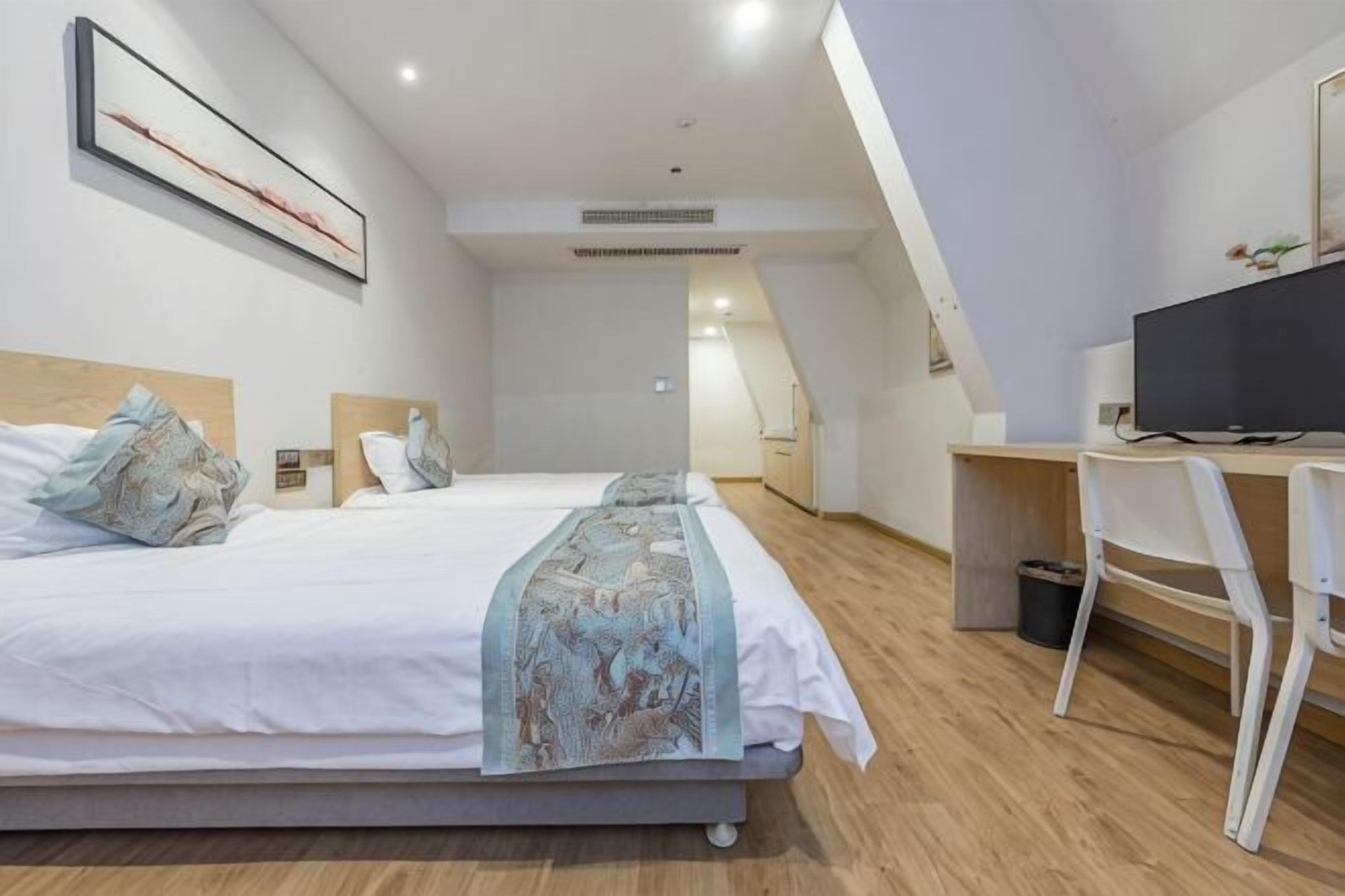 A bedroom with a bed, bedside tables, a desk, a chair, and a television.