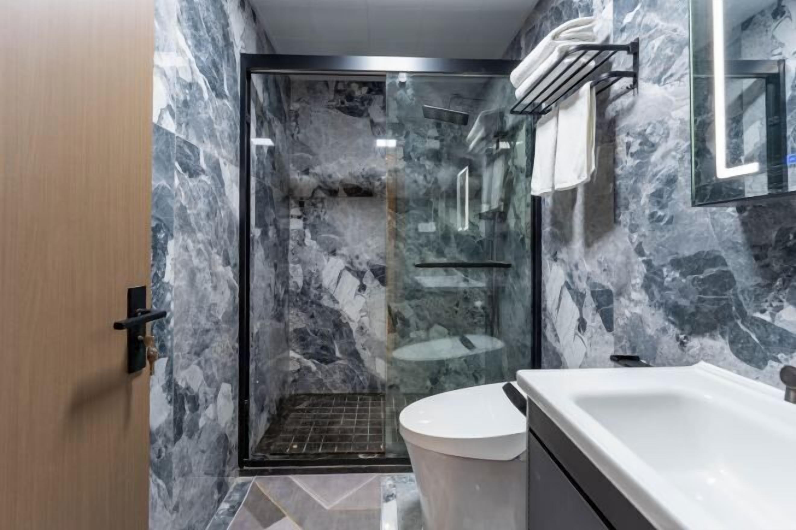 Une salle de bain moderne avec une douche à parois de verre, un lavabo blanc et un mur en marbre.