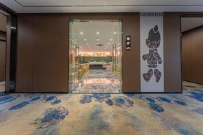 An interior view of a hotel lobby with a carpeted floor, a reception desk, and a wall with a cartoon bear illustration.
