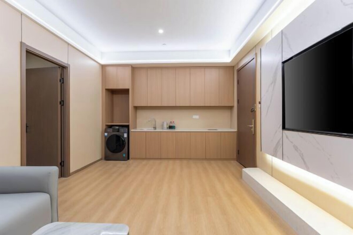 A modern kitchen with wooden cabinets, a built-in washing machine, and a large TV mounted on the wall.
