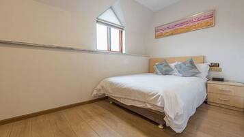 Un dormitorio con una cama individual, una mesita de noche, una ventana y un cuadro en la pared.