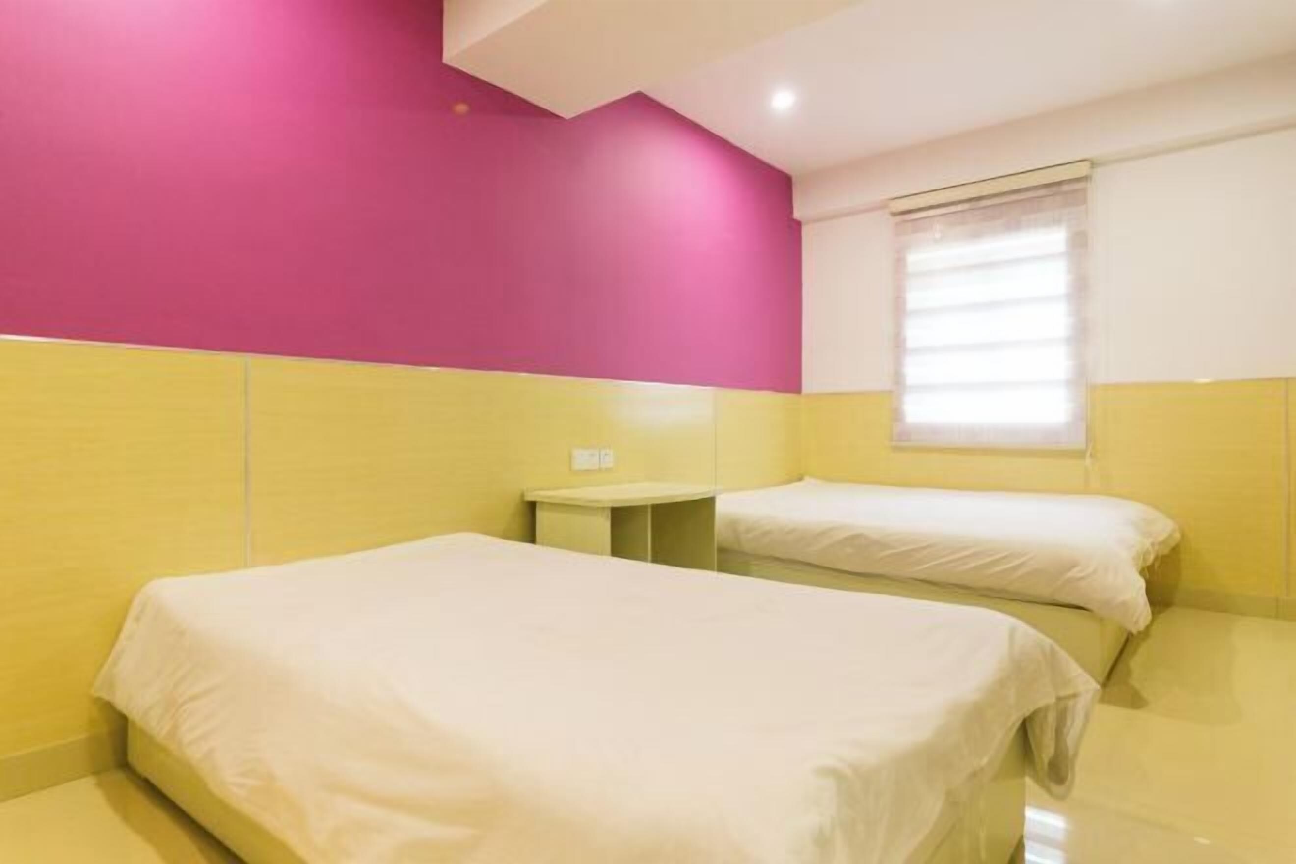 A hotel room with two beds, a small bedside table, and a window with blinds.