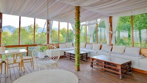 A spacious outdoor seating area with a wooden deck, white cushioned seating, and a hanging chair. - Hilltop Villa with Breathtaking Mountain Views - Sauna & Pool  (Zărnești)