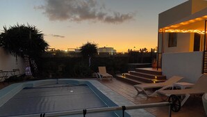 Ein Pool mit einer erhöhten Liegeinsel, umgeben von Liegestühlen und einer Treppe zu einer oberen Ebene.