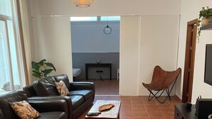 Ein Wohnzimmer mit einem Ledersofa, einem Holztisch, einem TV-Schrank und einem Esstisch.