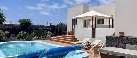 A swimming pool with lounge chairs and a covered seating area.