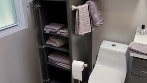 A compact bathroom with a toilet, a towel rack with folded towels, a trash bin, and a shelf with additional towels. - Dog friendly, peaceful 1 BR cottage w/ BA, AC on beautiful Lake Hodges (Escondido)