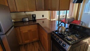 A compact kitchen with wooden cabinets, a stainless steel refrigerator, a gas stove, and a coffee maker. - Dog friendly, peaceful 1 BR cottage w/ BA, AC on beautiful Lake Hodges (Escondido)