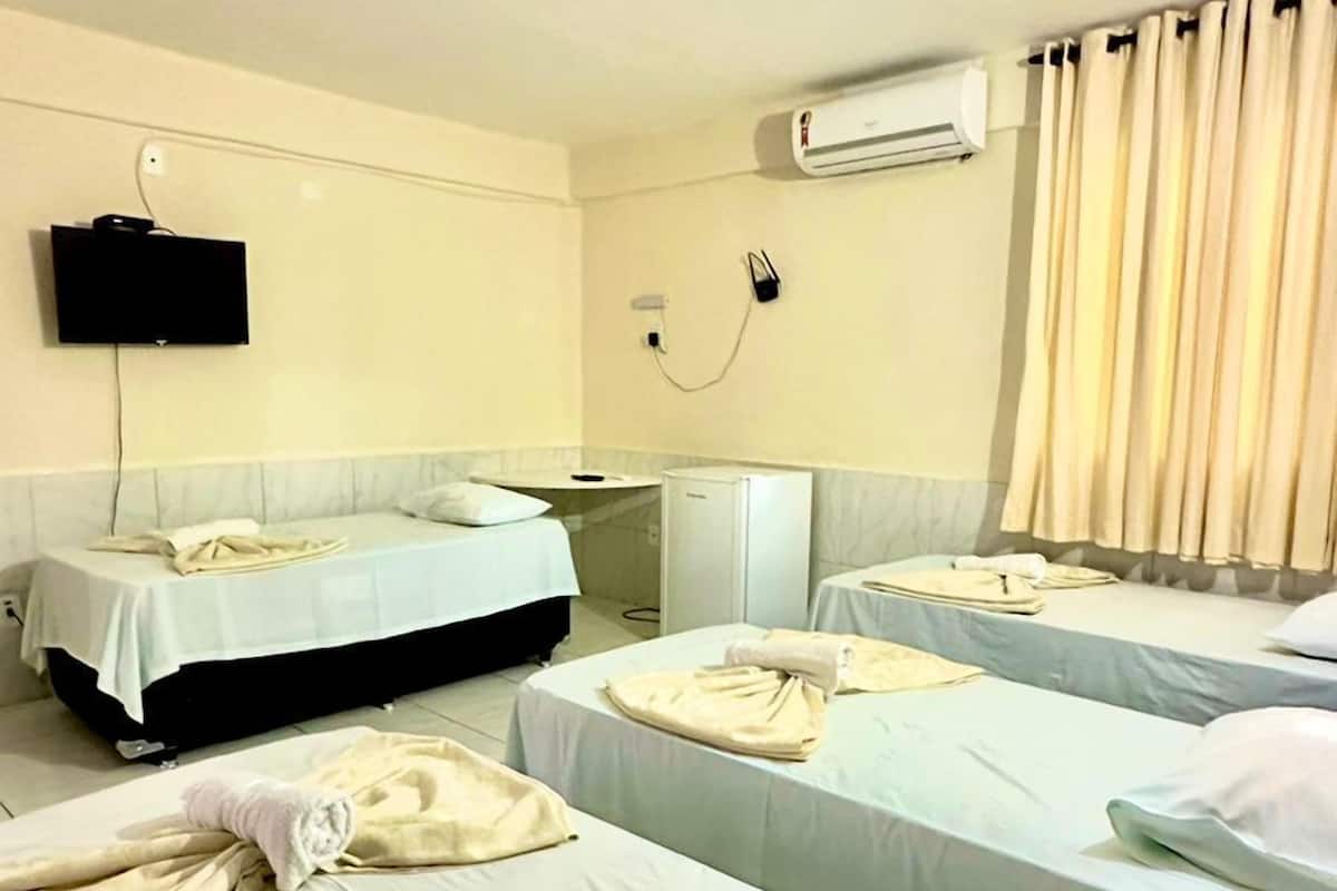 A hotel room with two single beds, a small desk, a television, and an air conditioning unit.