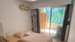 Une chambre à coucher comprenant un lit, un bureau, une bibliothèque et une porte-fenêtre coulissante donnant sur un balcon.