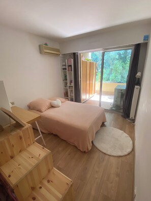 A bedroom with a bed, a desk, a bookshelf, and a sliding glass door to a balcony.