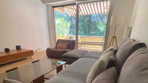 Un salon moderne avec un canapé, une table basse et un fauteuil. Une grande fenêtre offre une vue sur la verdure à l’extérieur.