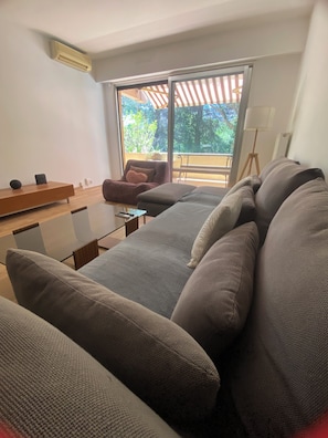 A modern living room with a sofa, a coffee table, and a chair. There is a large window with a view of greenery outside.