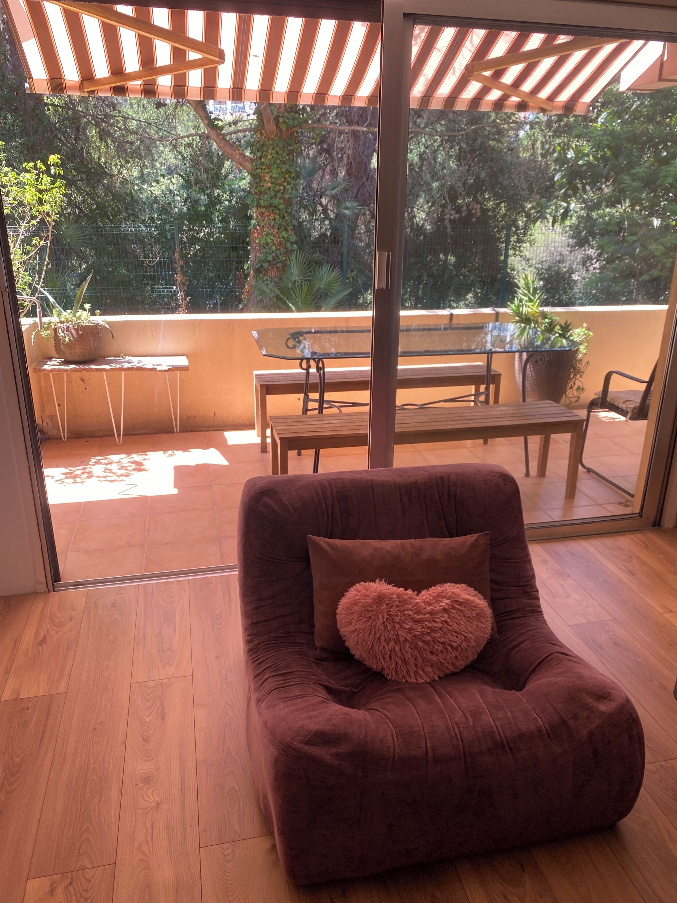 A cozy room with a brown sofa, a heart-shaped pillow, a glass table, and a bench.