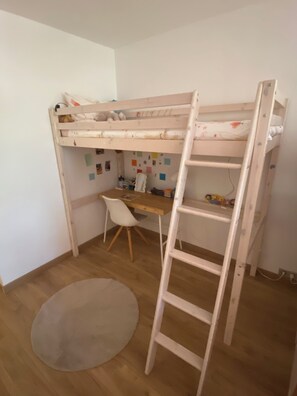 En køjeseng med skrivebord og stol, en stige og en rund måtte på et trægulv.
