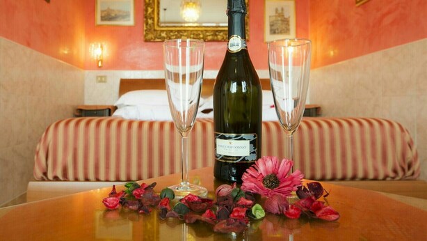 A hotel room with a bed, a bottle of wine, two glasses, and a table with flowers. - TERRAZZA SAN PIETRO EXCLUSIVE APARTMENT DE LUXE IN ROME  (Roma)