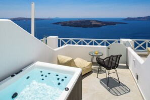 A balcony with a hot tub, a table with chairs, and a view of the sea and islands. - Elia Caldera Suites (Santorini)