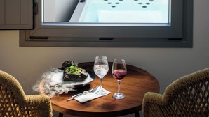 A balcony with a table, two chairs, a view of the sea, and a white chair with a cushion. - Elia Caldera Suites (Santorini)