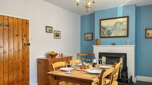 A dining room with a wooden table, chairs, a fireplace, and a blue wall.