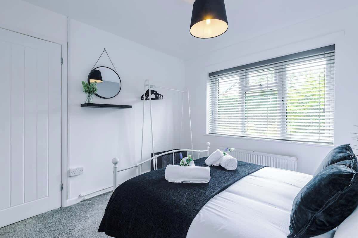 Une chambre à coucher moderne, avec un lit, une table de chevet, un miroir, un luminaire suspendu et une fenêtre avec des stores.
