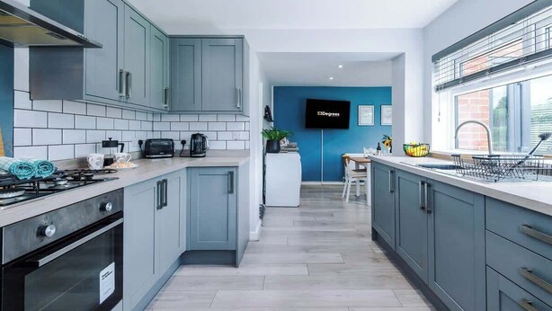 A modern kitchen with grey cabinets, a built-in oven, and a central island. - NEW! Stunning Bungalow, Ideal for Groups, Parking! (Wrexham)