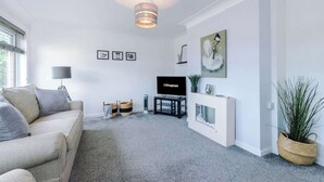 A modern living room with a sofa, TV, fireplace, and artwork on the wall. - NEW! Stunning Bungalow, Ideal for Groups, Parking! (Wrexham)