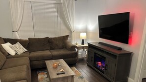 A living room with a sofa, coffee table, TV, fireplace, and a lamp. - Charming 2-bedroom condo, 15 min from city with laundry & parking (Boston)