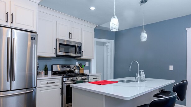 A modern kitchen with stainless steel appliances, white cabinetry, a central island, and black bar stools. - Charming 2-bedroom condo, 15 min from city with laundry & parking (Boston)