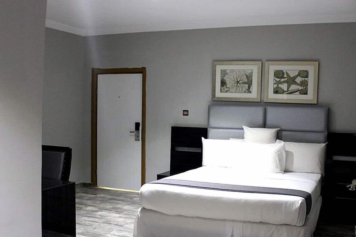Hotellihuone, jossa on sänky, yöpöytä, televisio ja kaksi kehystettyä taideteosta seinällä.