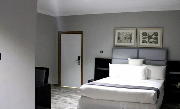 A hotel room with a bed, a bedside table, a TV, and two framed artworks on the wall. - Ellyxville Hotel (Lekki)